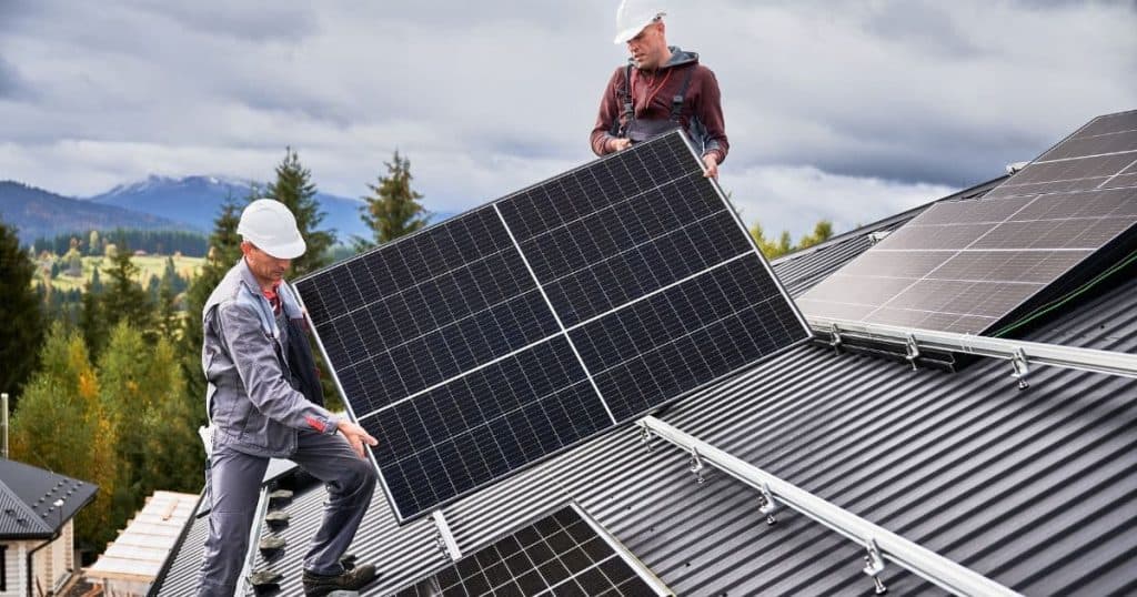 deux installateurs de panneaux solaires sur un toit qui portent un panneau solaire