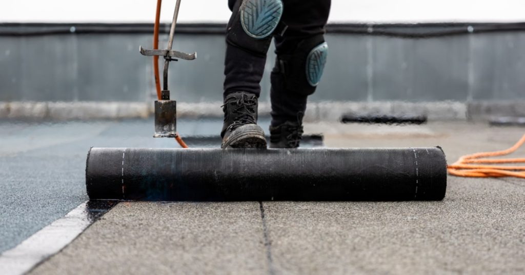 Ouvrier qui installe une couche de EPDM sur un toit plat, avec un rouleau et des câbles sur le coté. 