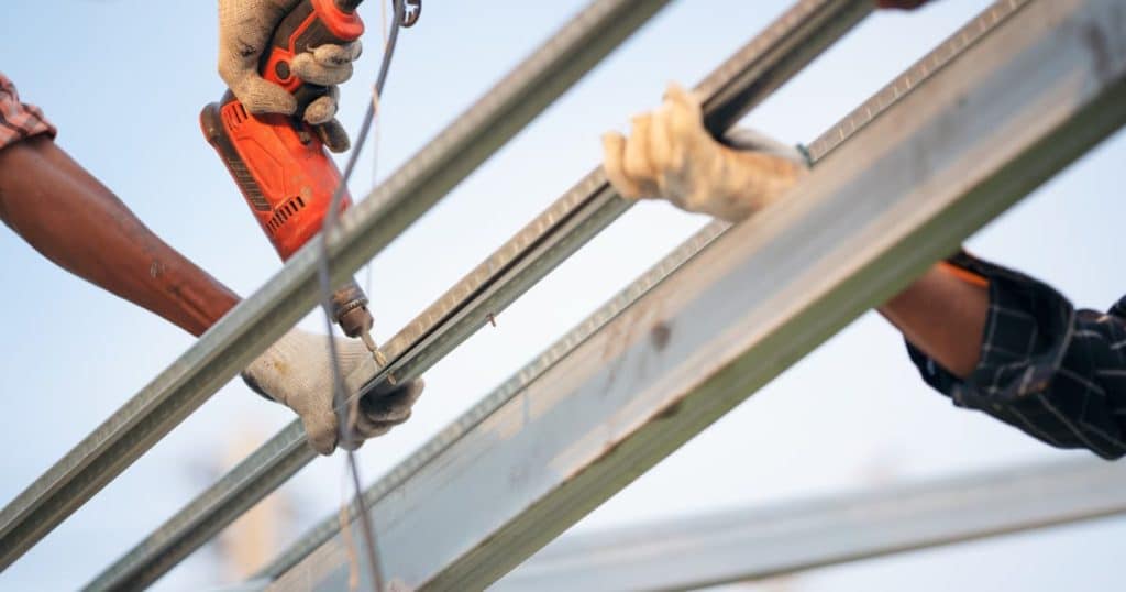 Travaux de construction avec une main entrain de percer du bois et deux autre qui tiennent la barre. 