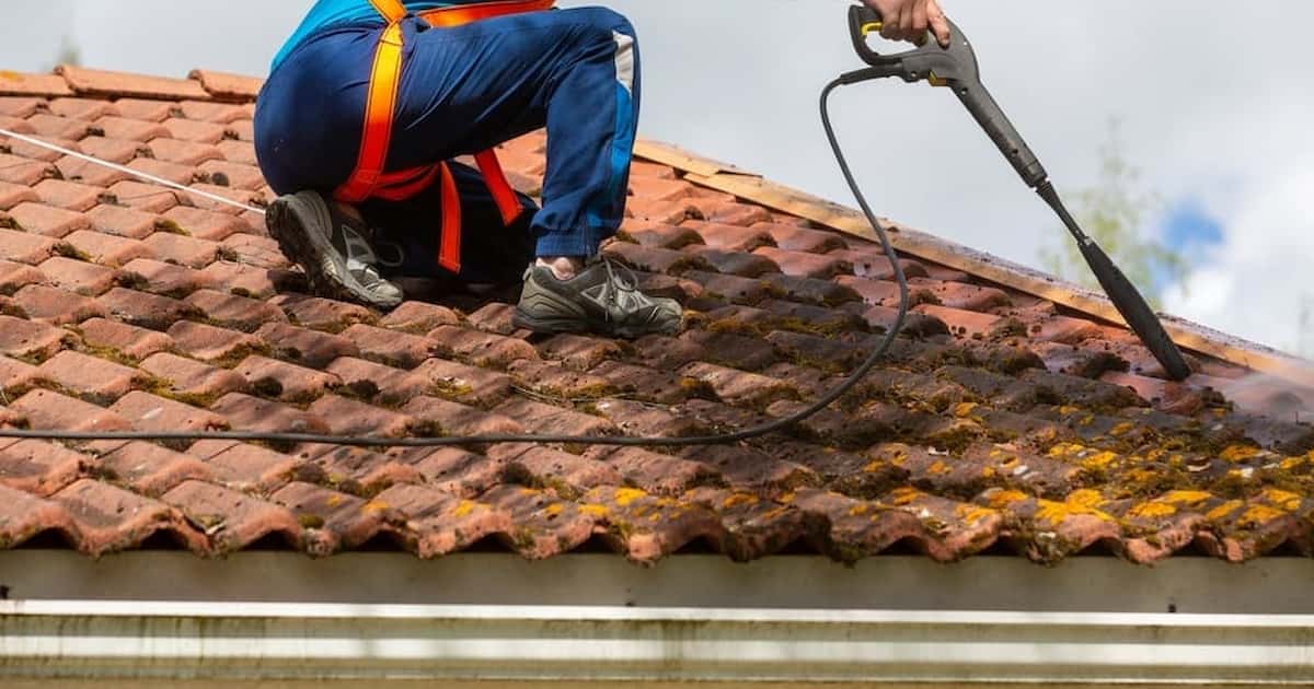 Professionnel en train de démousser un toit avec un arroseur à haute pression