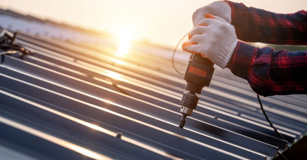 Un ouvrier fixe des tôles d'acier sur un toit avec une visseuse. 