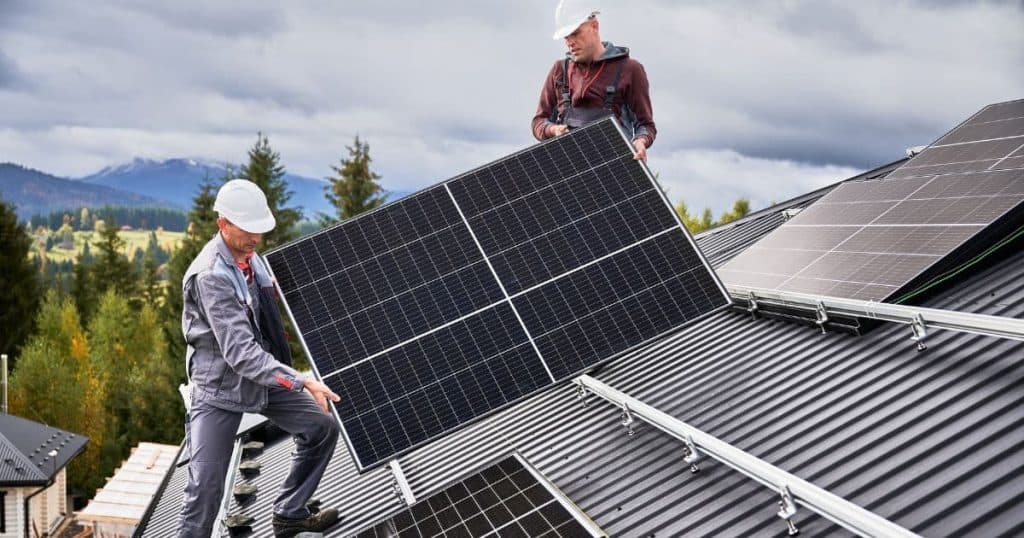 deux installateurs de panneaux solaires sur un toit qui porte un panneau solaire