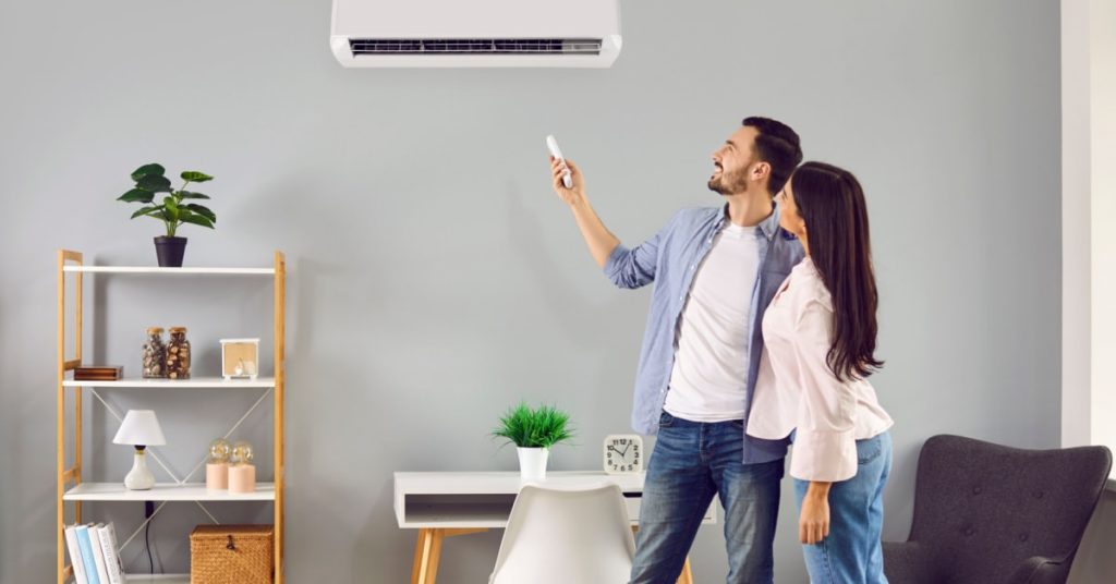 Jeune couple utilise un climatiseur dans leur salon pour avoir de l'air frais. 