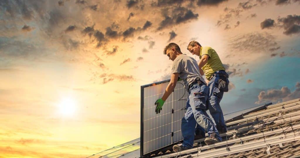 2 hommes sur un toit transportant une lucarne en plein couché de soleil.