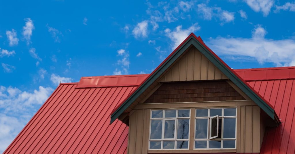 Toiture en acier rouge, avec deux fenêtres et une façade en bois. 