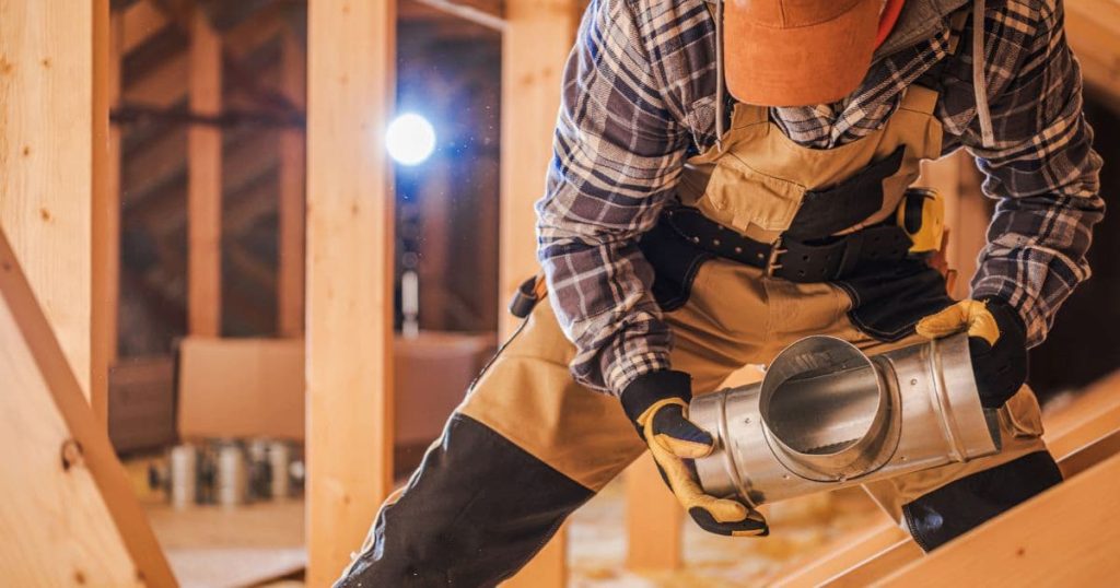 Ouvrier en salopette de chantier avec casquette orange et chemise à carreaux qui pose un cylindre métallique dans la charpente