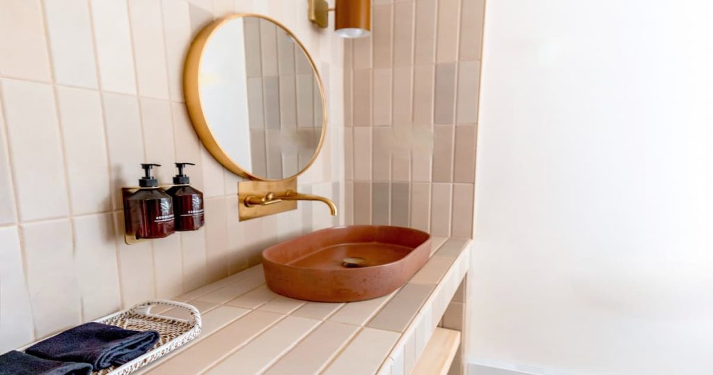 salle de bain avec évier, miroir et savons avec un carrelage aux tons neutres