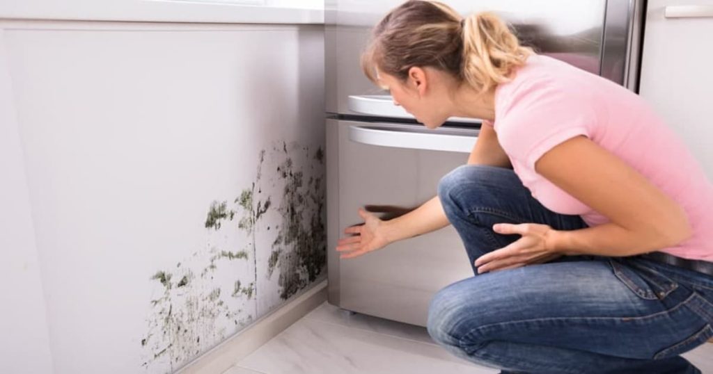 Femme inquiète face au mur de sa cuisine avec des tâches de moisissures