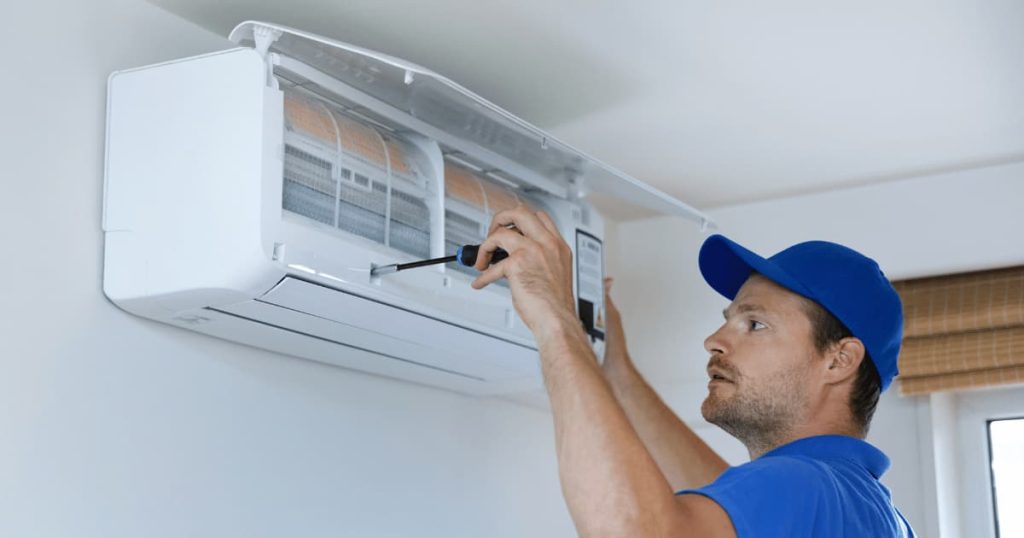 Chauffagiste avec une casquette bleu  qui répare l'unité intérieur de la pompe à chaleur