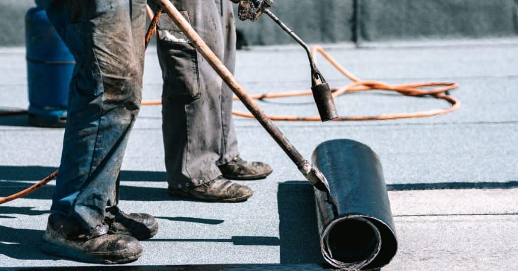 ouvriers qui installent une membrane d'étanchéité bitumeuse sur un toit plat 