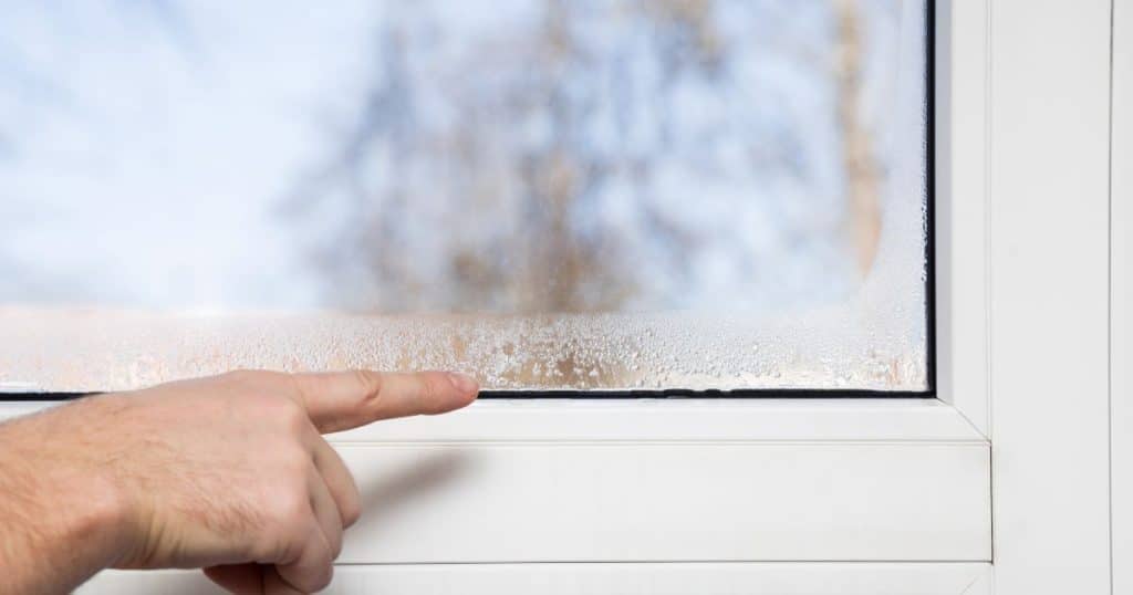 doigt d'une main qui pointe vers la condensation sur une fenêtre d'appartement 