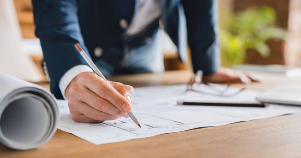 Un homme surplombe une table et annote un plan de maison