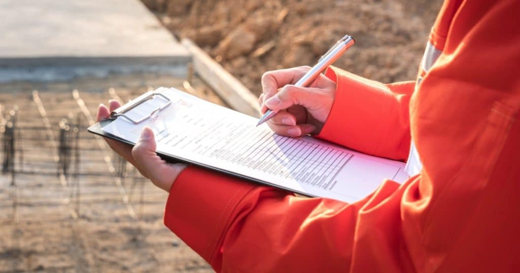 Une personne en tenue de chantier prend des notes sur un document 