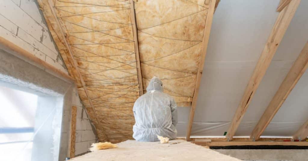 Homme isolant une toiture par l'intérieur à l'aide de matelas isolants