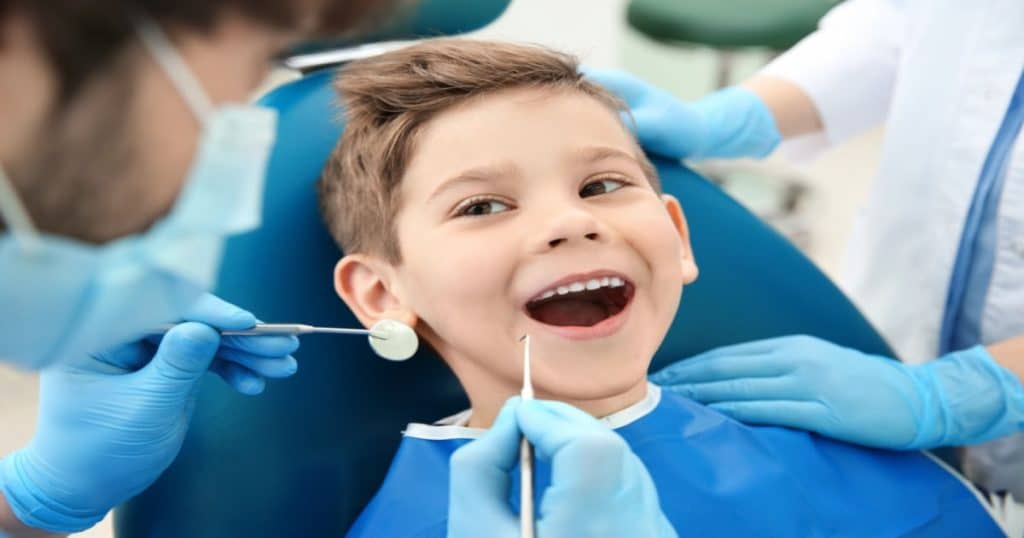 Un garçon sourit en montrant ses dents au dentiste qui s'apprête à l'examiner. 