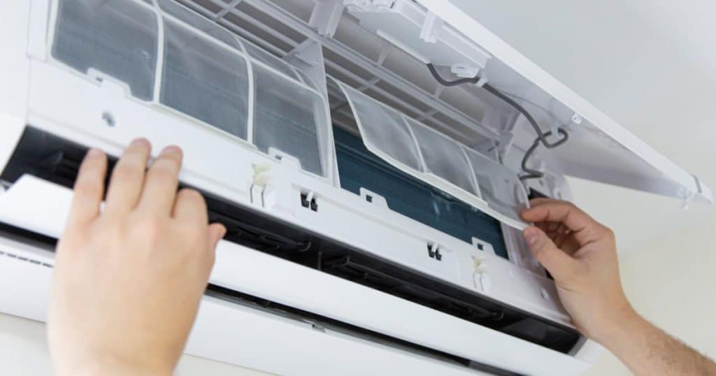 Les mains d'un technicien remettent les filtres d'une pompe à chaleur en place après nettoyage. 