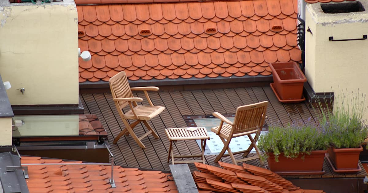 une terrasse avec deux chaises et une table en bois sur un toit plat , entouré de toiture en pente