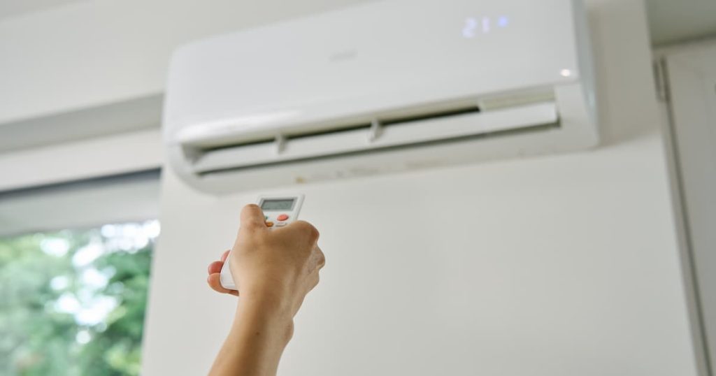 Hand met afstandsbediening die airco toestel aan zet. 