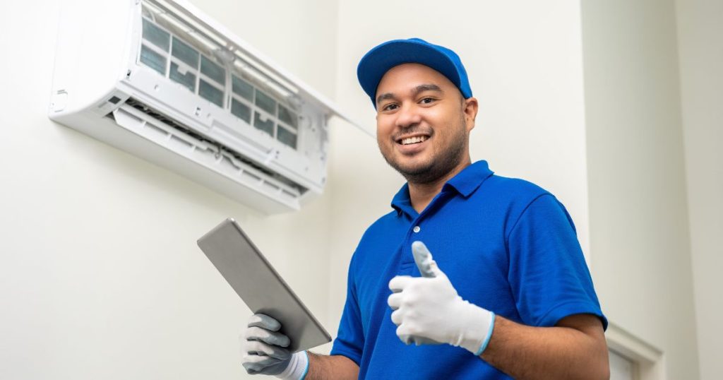 Ervaren airco installateur draagt blauwe werkkledij en oordeelt dat de nieuwe airco succesvol geïnstalleerd is 