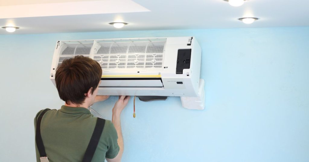 Jonge specialist plaatst de binnenunit van een airco tegen een blauwe muur 