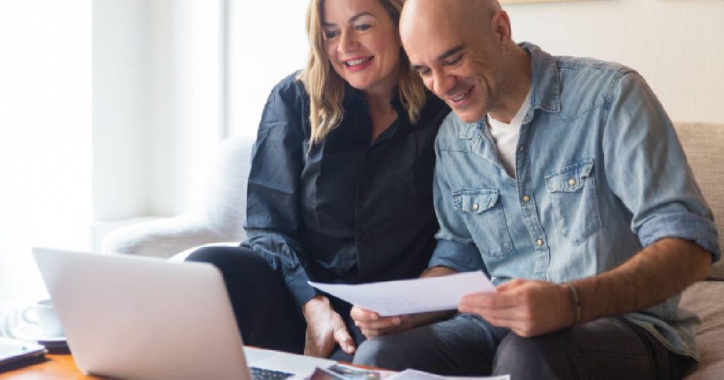 Een man en een vrouw zitten achter een computer en regelen online de aanvraag van de Mijn VerbouwPremie en de Mijn VerbouwLening voor het energetisch renoveren van hun woning.