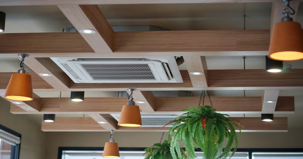 De binnenunit van een design airco in plafondmodel, stijlvol verwerkt tussen de decoratieve houten plafondbalken.