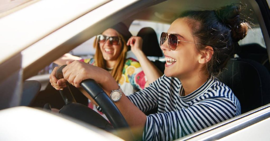 Twee jonge vrouwen in een witte auto, gedekt door de goedkoopste autoverzekering in België voor hun persoonlijke situatie. 