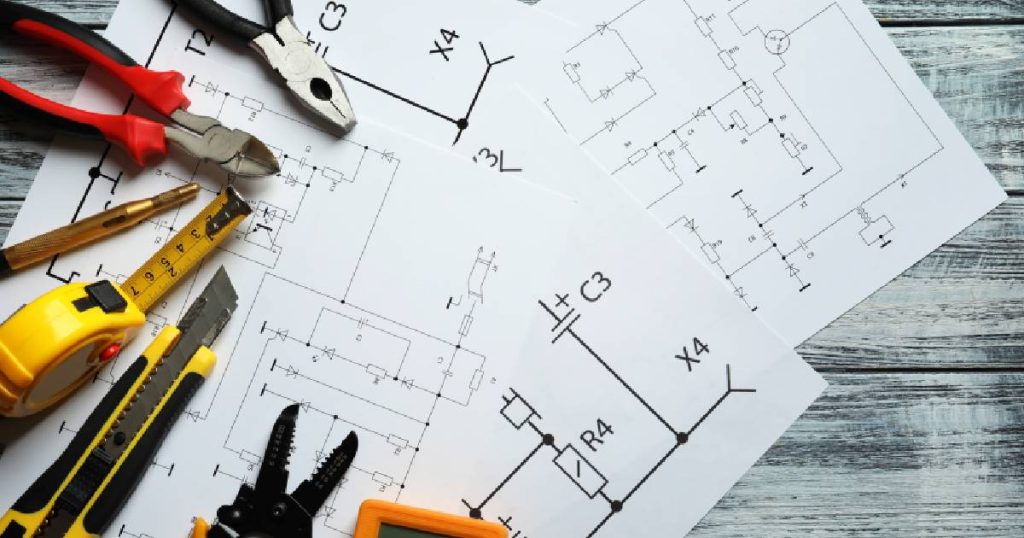 Elektrische schema's van een laadpaal die volgens het AREI werd geïnstalleerd. Op de schema's liggen verschillende stukken gereedschap: een rolmeter, knijptangen en een breekmes.