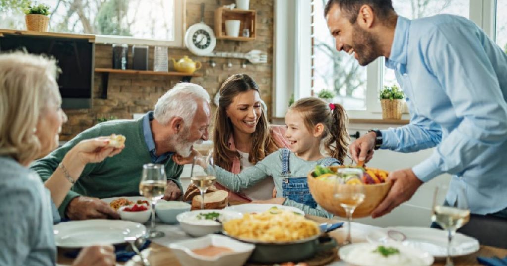 Een groot gezin aan tafel bestaande uit een grootmoeder, grootvader, moeder, dochter en vader. Aangezien zij samen op eenzelfde adres gedomicilieerd zijn, valt elk van hen onder dezelfde familiale verzekering.