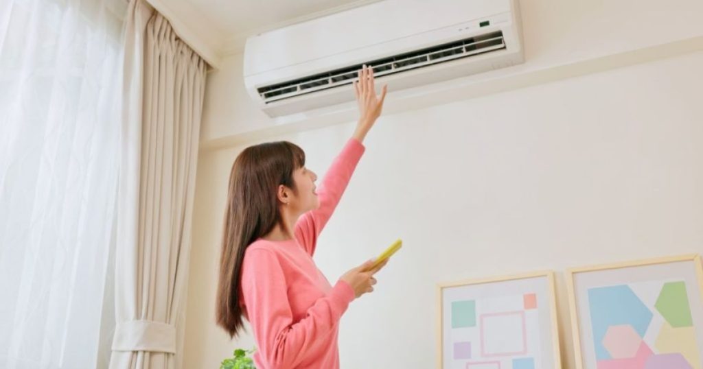 Een vrouw die een airco op temperatuur test