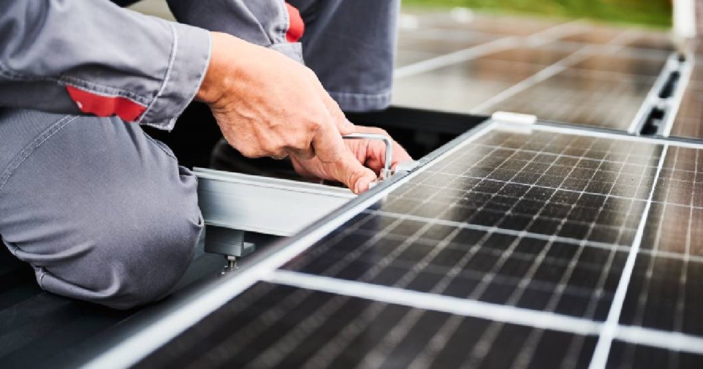 Een man in een lichtgrijze overall installeert zonnepanelen voor bedrijven.