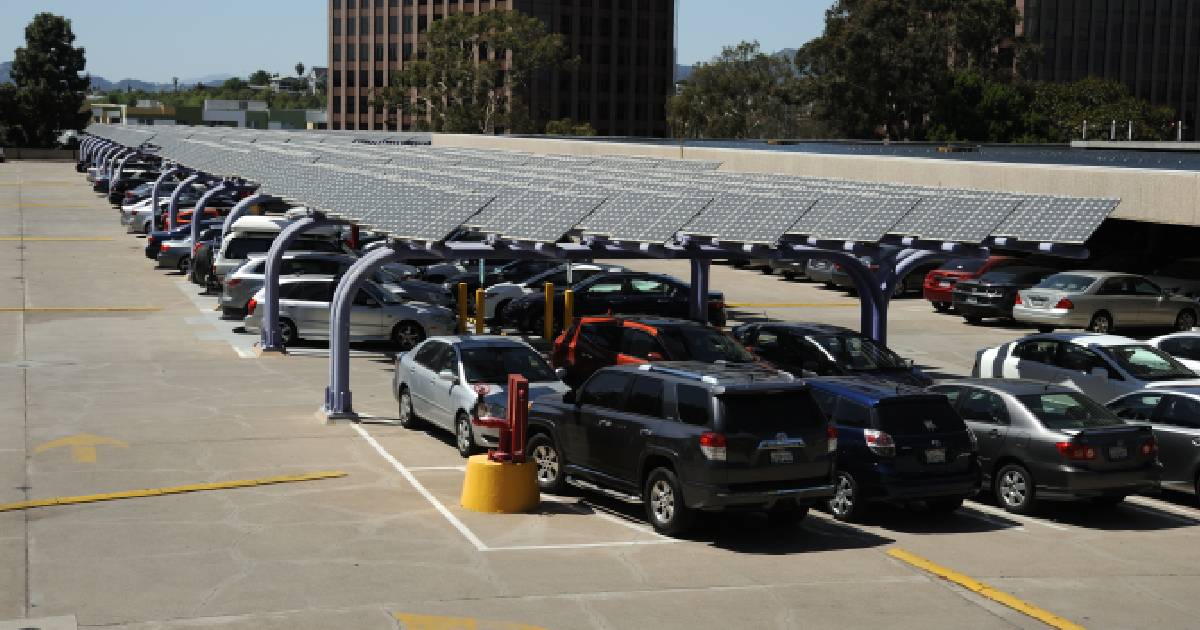 Een groot parkeerterrein met carports met zonnepanelen en laadpunten voor elektrische wagens voor de werknemers en klanten van de omliggende bedrijven.