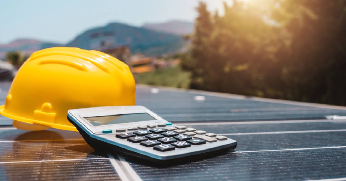 Un toit avec des panneaux solaires pour les entreprises sur lequel se trouvent un casque jaune et une calculatrice.