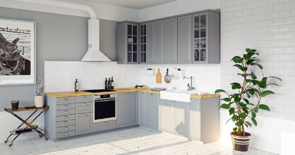 Een minimalistische keuken in Scandinavische stijl met witte metrotegels, grijze keukenkasten en ingebouwde keukenapparatuur. Een klein bijzettafeltje met een kamerplant en een grote potplant in de hoek van de ruimte geven de keuken een natuurlijke toets. Het houten werkblad en de witte, porseleinen spoelbak zijn duurzaam, functioneel en stijlvol.