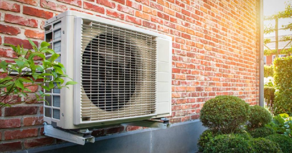 De buitenunit van een airco die met montagebeugels laag boven de grond tegen een gevel is geïnstalleerd: ideaal voor een woning met vloerairco.