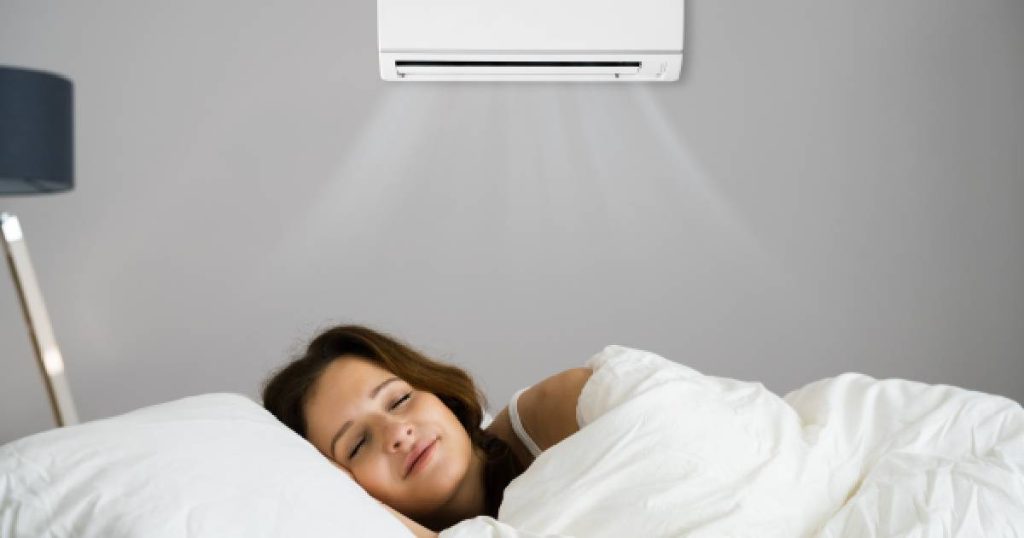 Een vrouw ligt vredig te slapen in een ruimte met een mobiele split airco die aan de wand bevestigd is. 