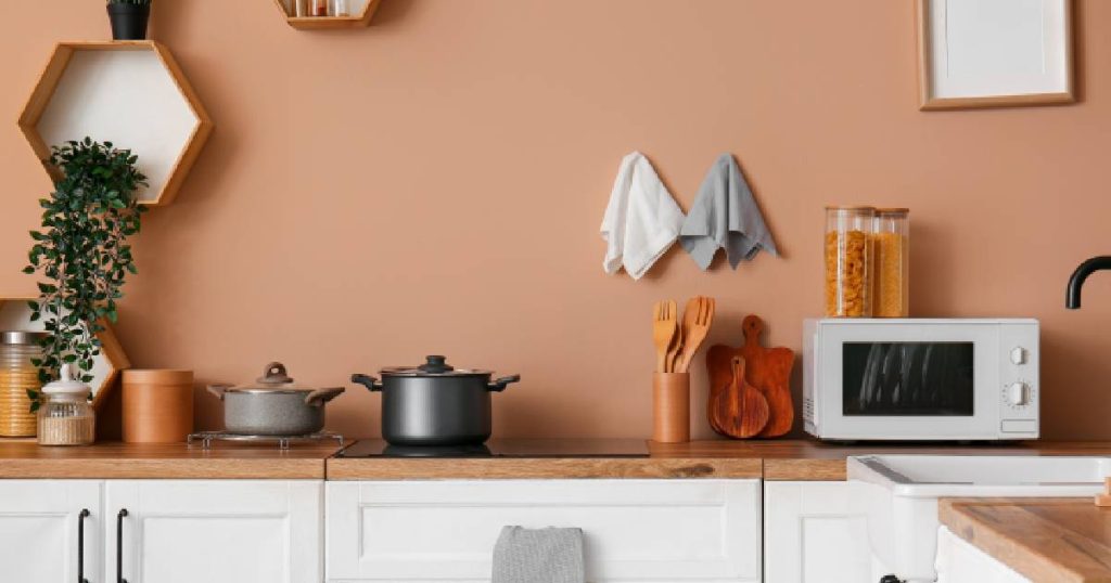 Een vrolijke boho-keuken met beige wanden met diepe, oranje ondertoon, witte keukenkasten, een houten aanrechtblad en verschillende accessoires op het aanrechtblad.