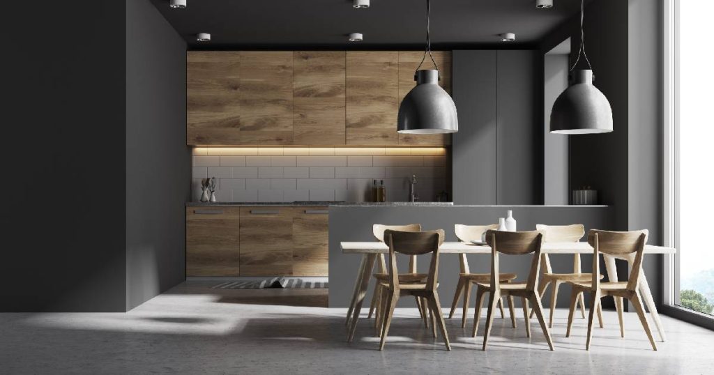 Een moderne keuken met vloer in betonlook die glanzend werd afgewerkt, grote moderne lampen, houten keukenkasten en een grote eettafel met 6 stoelen. 