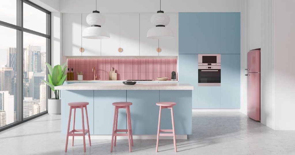 Een trendy witte keuken met blauwe en roze oppervlakken. Een lichtblauw keukeneiland met roze stoeltjes oogt speels en gezellig. De roze ingebouwde koelkast en de roze spatwand achter het aanrechtblad geven de keuken een eigenwijze uitstraling.