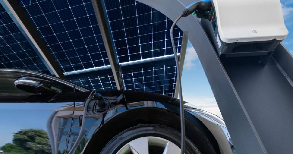 Een moderne stalen carport met zonnepanelen en een laadpaal voor een elektrische auto.