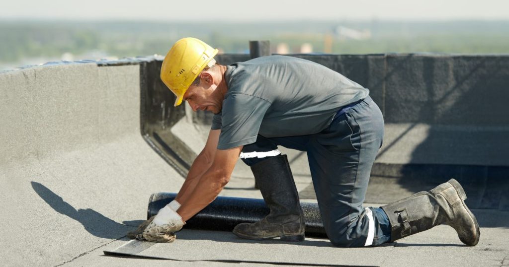 Een dakwerker plaatst nieuwe dakisolatie op een omgekeerd plat dak: het isolatiemateriaal fungeert zowel als isolatie als als dakbedekking.