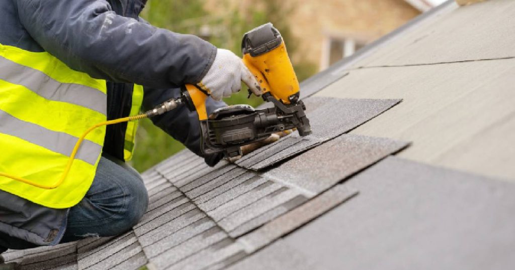 Een dakwerker bevestigt een dakshingle uit dakleer (bitumen of roofing) op een hellend dak.