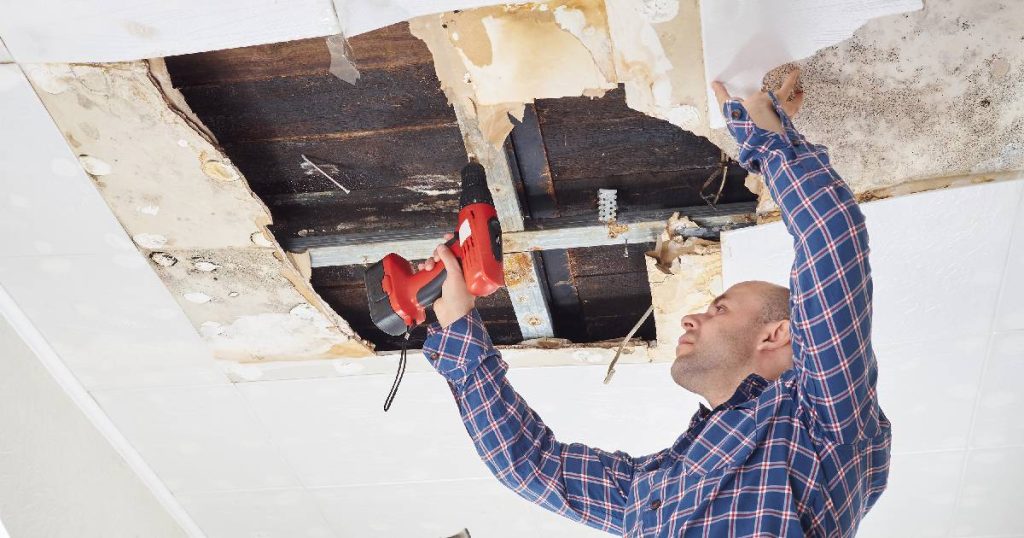 Een vakman met geruit hemd repareert de waterschade aan een plafond na een daklekkage. 