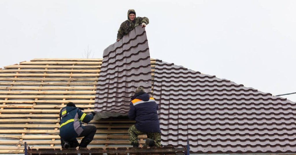 Drie dakspecialisten werken samen om een dakpanplaat met isolatie op de panlatten van een dak te leggen.