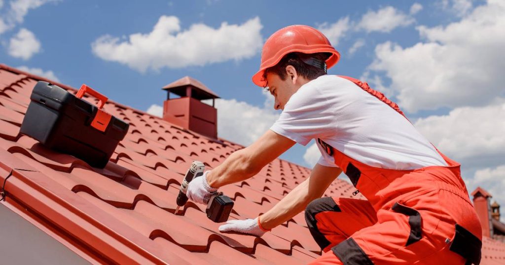 Een dakwerker bevestigt rode of terracotta kunststof dakpanplaten met isolatie met schroeven op het dak van een woning.