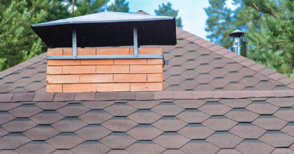 Een dak waarop de eigenaars van de woning dakshingles hebben laten plaatsen. Uit het dak steekt een bakstenen schouw.