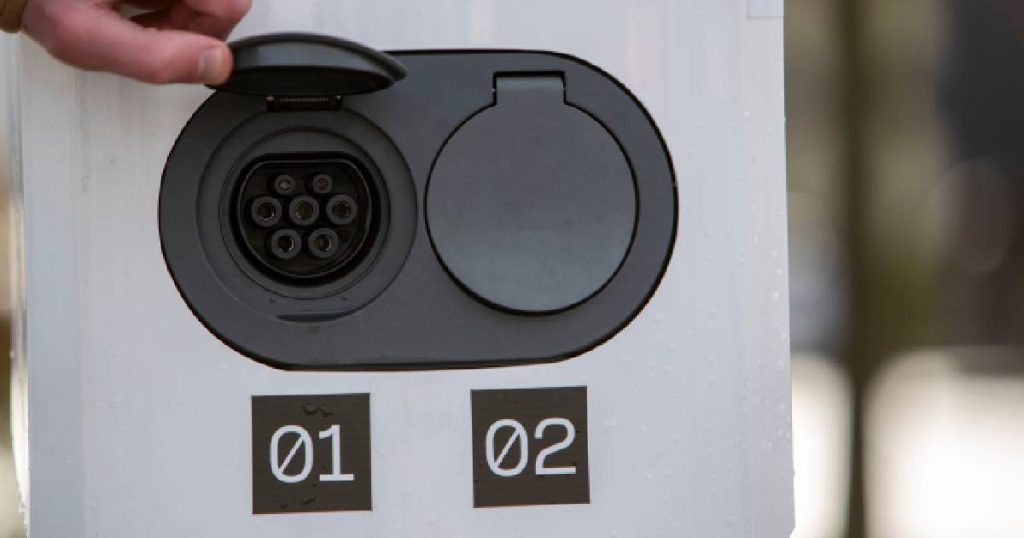 Een grijze, dubbele laadpaal of dubbel socket laadstations met 2 zwarte aansluitingen voor losse laadkabels van elektrische voertuigen. De sockets zijn genummerd.
