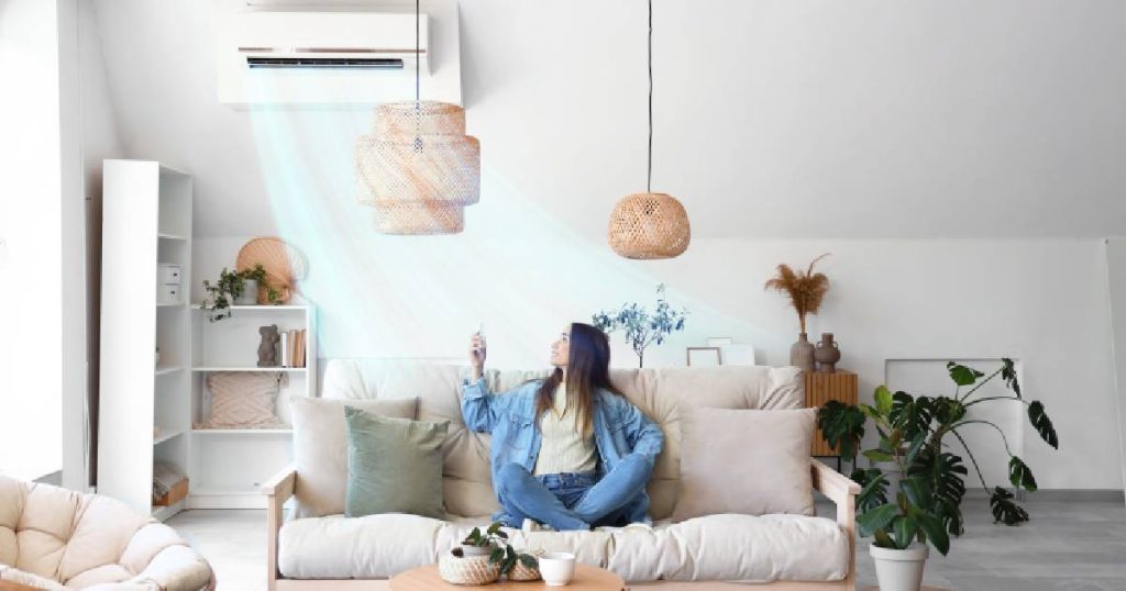 Een dame met blauwe jeans, blauw hemdje en lichtgeel t-shirt zet haar airco systeem op met een druk op de knop.