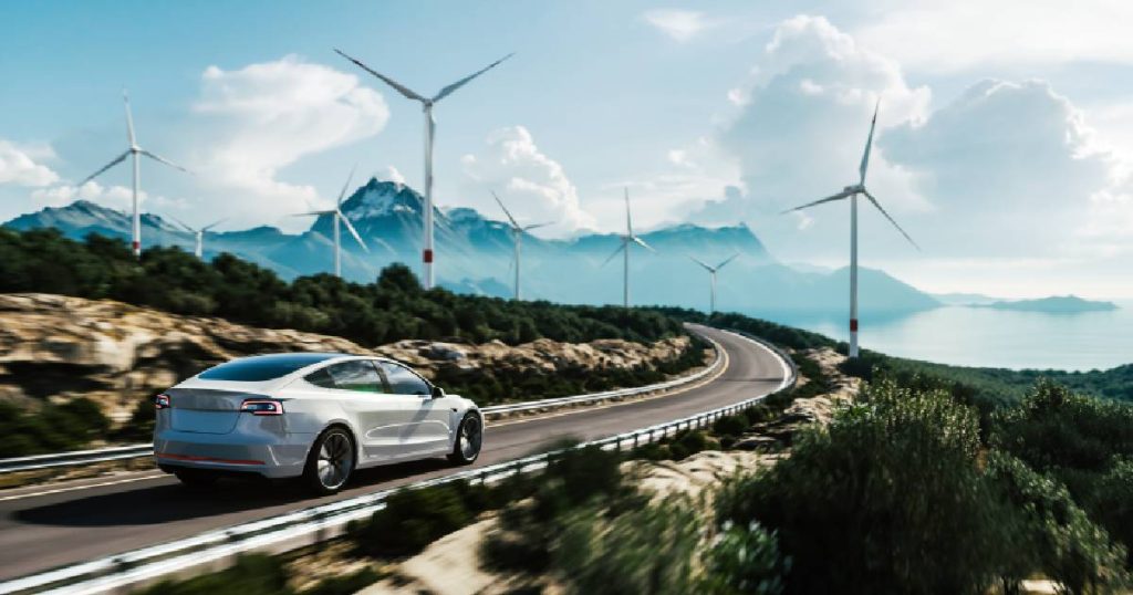 Een elektrische wagen waarvoor een premie werd ontvangen op een openbare weg, op de achtergrond windmolens, bergen, een meer en wolken.