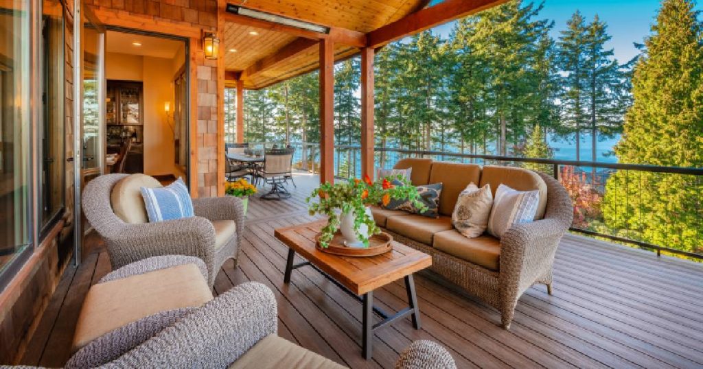 Een half gesloten veranda met uitzicht op een bos. De veranda is erg ruim en ingedeeld in een zitgedeelte met loungeset en een gedeelte met een tafel en stoelen. De vloer bestaat uit houten planken.